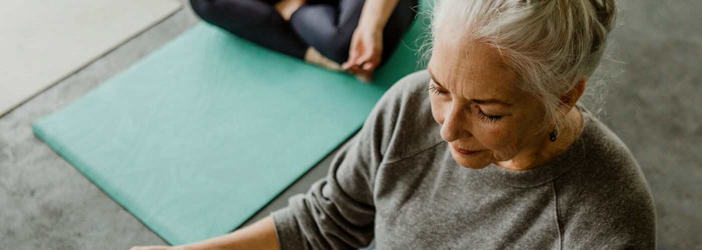 Eine ältere Frau mit hochgestecktem grauem Haar praktiziert Yoga